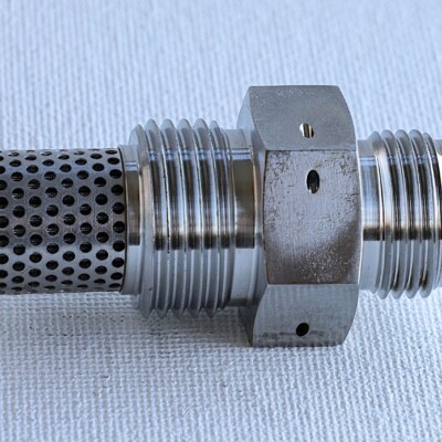 A metal hydraulic filter fitting with a hexagonal nut and a perforated mesh filter end, placed on a white surface.